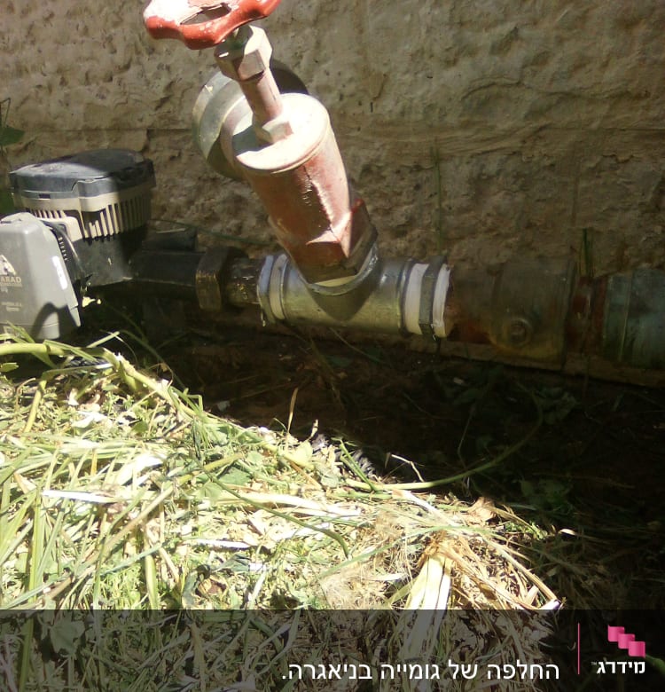 שסתום מים עם ידית אדומה וצינור מתכת